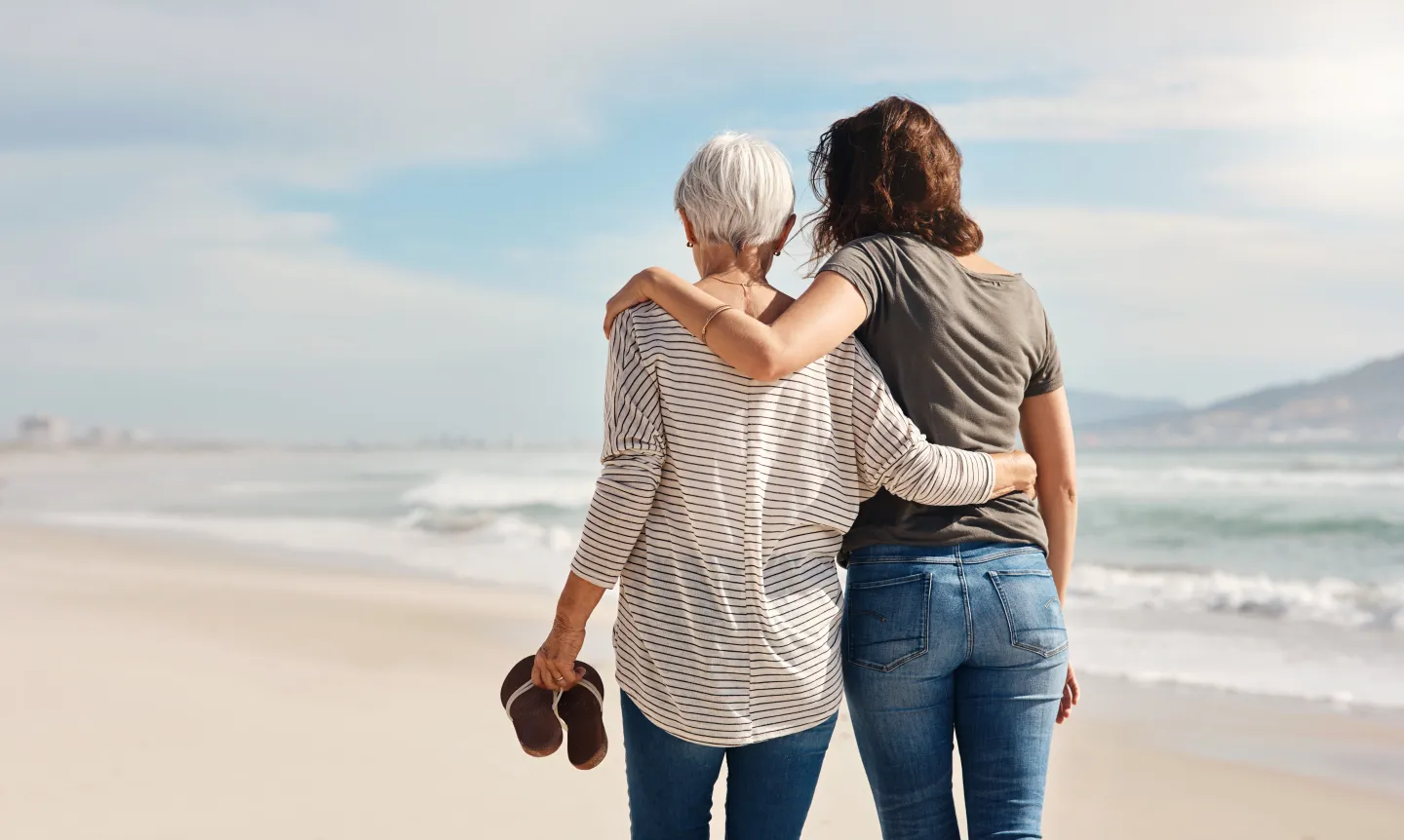 Zwei Frauen laufen im Arm am Strand entlang. Blogbild zum Thema: Trauerprozess
