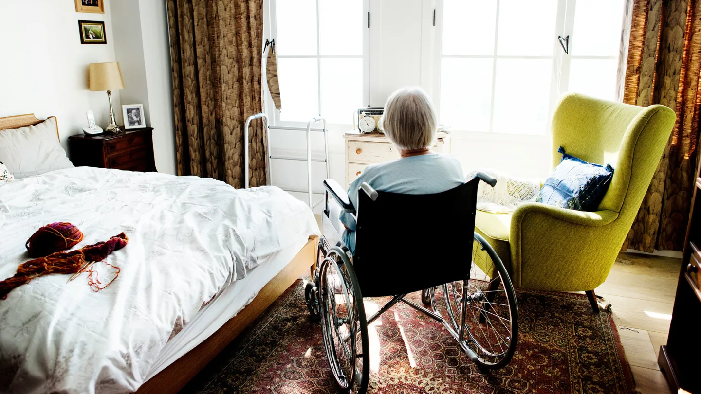 Eine Seniorin sitzt im Rollstuhl am Fenster. Man sieht sie nur von hinten.