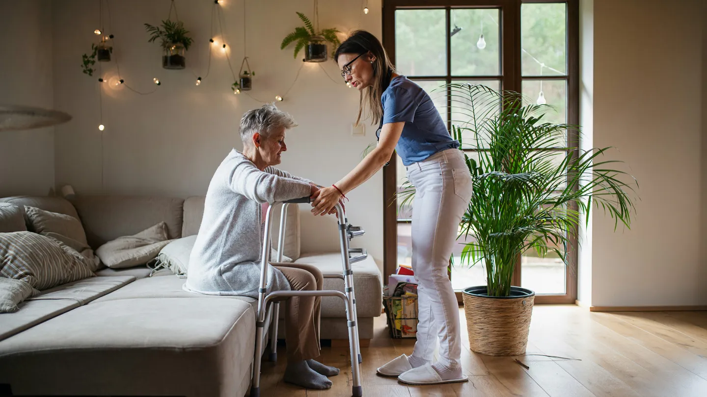 Eine Pflegerin hilft einer Seniorin beim Aufstehen.